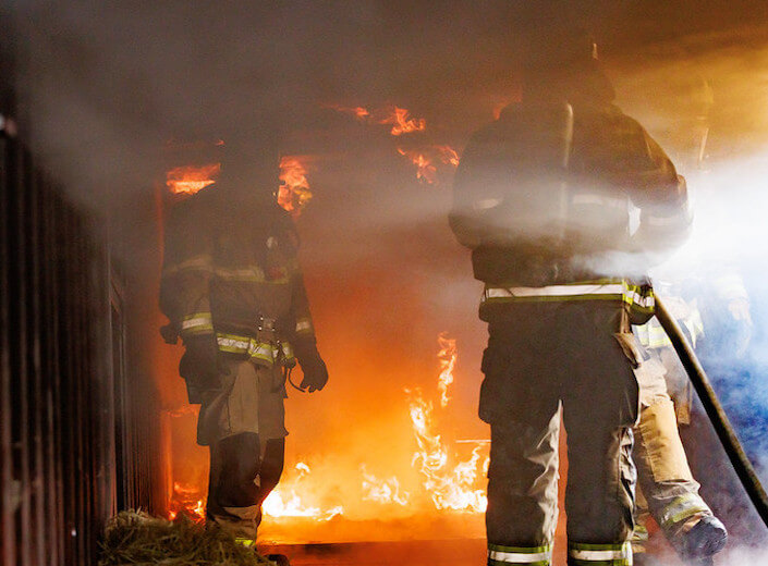 Fire Academy practice burn. Two figures in their uniforms are silhouetted against the smoke and fire.