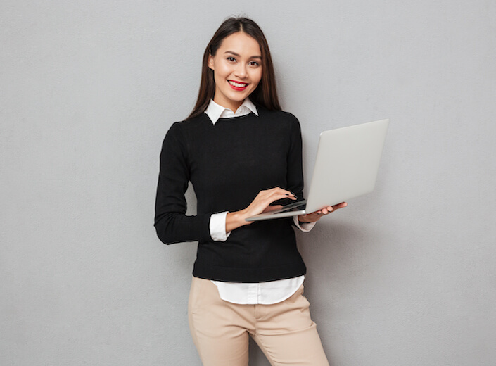 Young woman with straight dark hair and sweater holds a laptop.