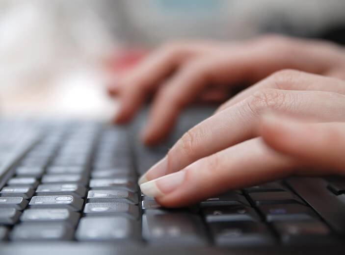 A woman's fingers type on a keyboard.