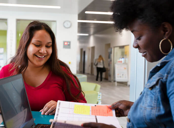 two female students looking at book in lounge