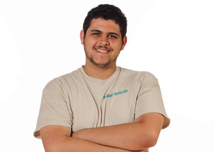 Young man in a light brown Mission Tshirt poses for a photo. He has light brown skin and black hair. He is in his late teens or early twenties.