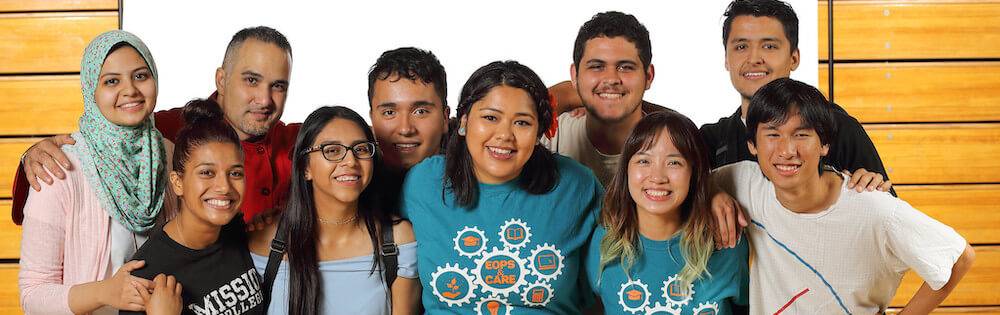 Students posing in group. Group of about ten students, mostly female, some male and of various ethnicities pose in a photo studio. They are in their twenties.