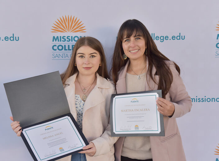 Two female Puente graduates holding certificates at a commencement ceremony for PUENTE.